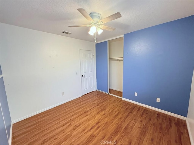 unfurnished bedroom featuring ceiling fan, a closet, a textured ceiling, and hardwood / wood-style floors