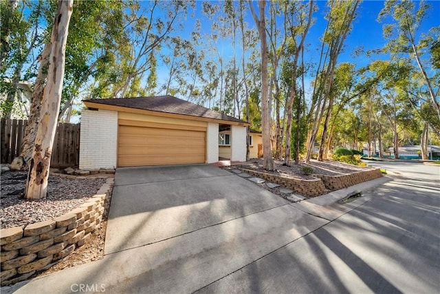 exterior space featuring a garage, fence, brick siding, and driveway