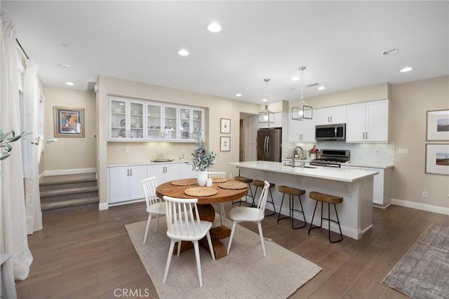 kitchen featuring decorative light fixtures, white cabinetry, stainless steel appliances, and an island with sink