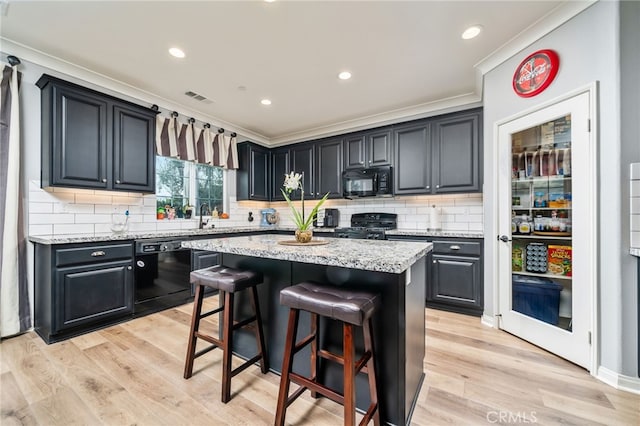 kitchen with black appliances, crown molding, a breakfast bar area, and a kitchen island