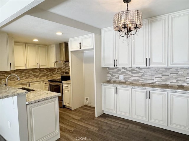 kitchen featuring an inviting chandelier, stainless steel electric range, hanging light fixtures, wall chimney range hood, and white cabinets