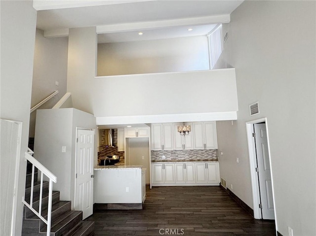 interior space featuring white cabinetry, backsplash, dark wood-type flooring, a towering ceiling, and wall chimney exhaust hood