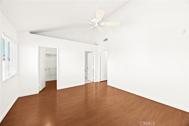 unfurnished bedroom with ceiling fan, vaulted ceiling, dark hardwood / wood-style floors, a walk in closet, and a closet