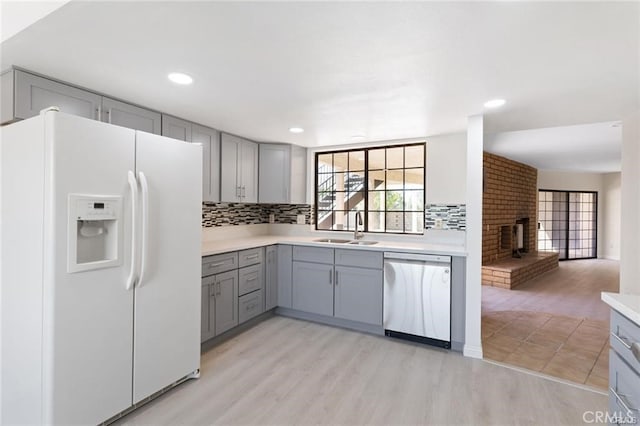 kitchen featuring dishwasher, white refrigerator with ice dispenser, light hardwood / wood-style floors, sink, and gray cabinetry