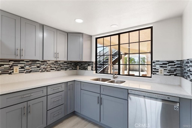 kitchen featuring light stone countertops, gray cabinets, stainless steel dishwasher, and sink