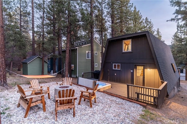 back of property featuring a gambrel roof, an outdoor fire pit, roof with shingles, a deck, and an outbuilding