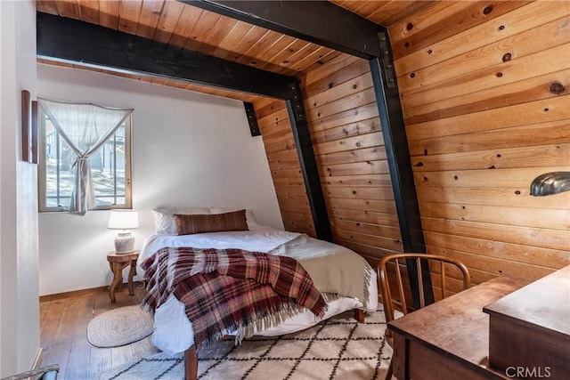 bedroom with beam ceiling, hardwood / wood-style flooring, wooden walls, wooden ceiling, and baseboards