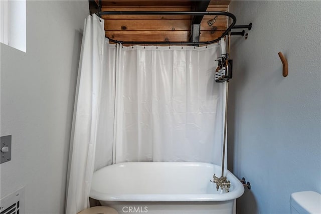 bathroom featuring toilet, a freestanding bath, and a shower with shower curtain