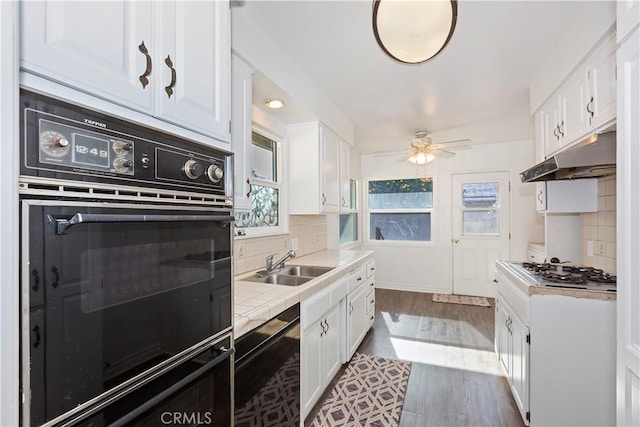 kitchen with sink, tasteful backsplash, tile countertops, black appliances, and white cabinets