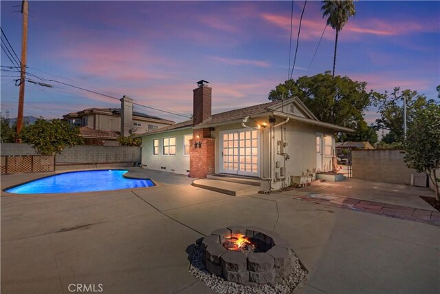 pool at dusk with an outdoor fire pit, an outdoor structure, and a patio