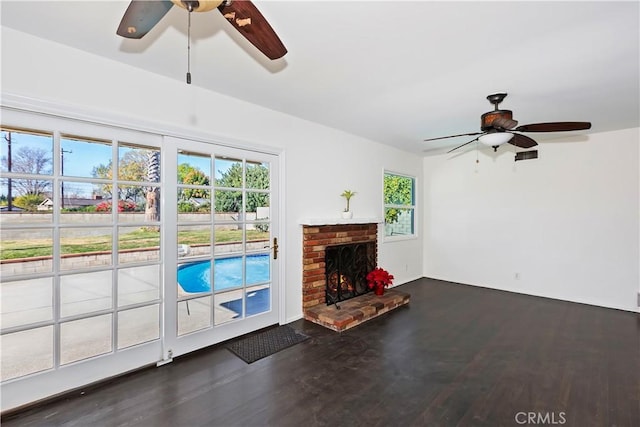 unfurnished living room with ceiling fan, a brick fireplace, and dark hardwood / wood-style flooring