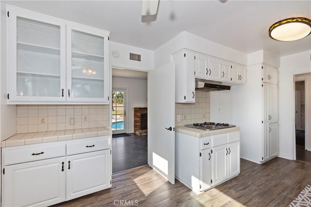 kitchen featuring stainless steel gas stovetop, tile counters, white cabinets, and backsplash