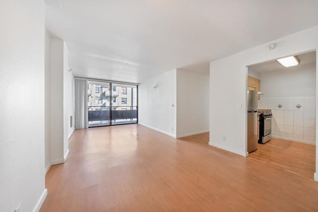 unfurnished room featuring a wall of windows, light hardwood / wood-style flooring, and tile walls