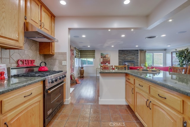 kitchen with decorative backsplash, dark stone counters, high end stove, and a healthy amount of sunlight