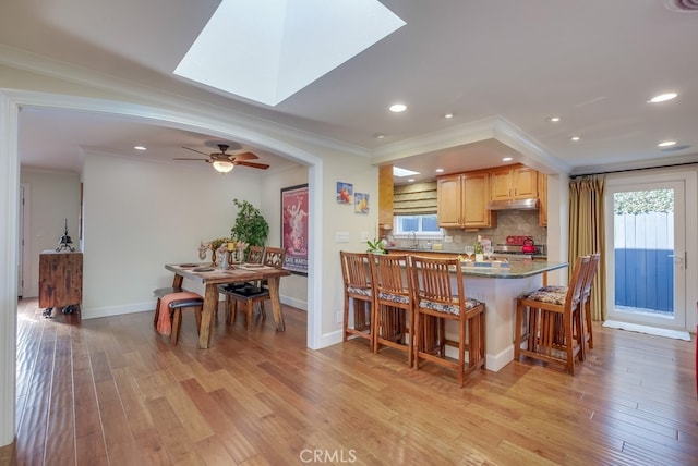 kitchen with a skylight, decorative backsplash, crown molding, and light hardwood / wood-style flooring