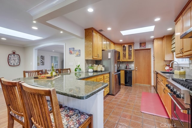 kitchen featuring a skylight, kitchen peninsula, stainless steel appliances, a kitchen breakfast bar, and dark stone counters