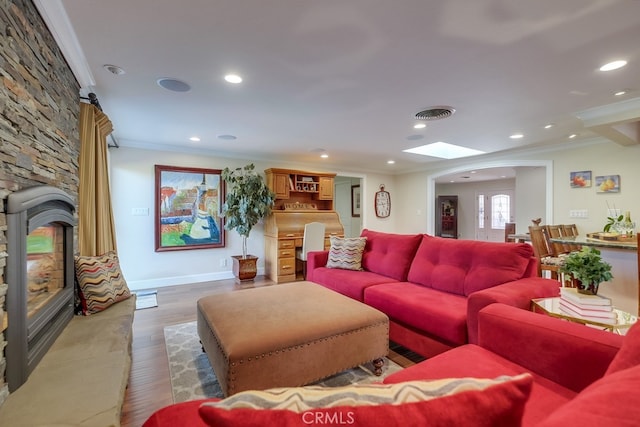 living room featuring dark wood-type flooring, a skylight, crown molding, and a stone fireplace