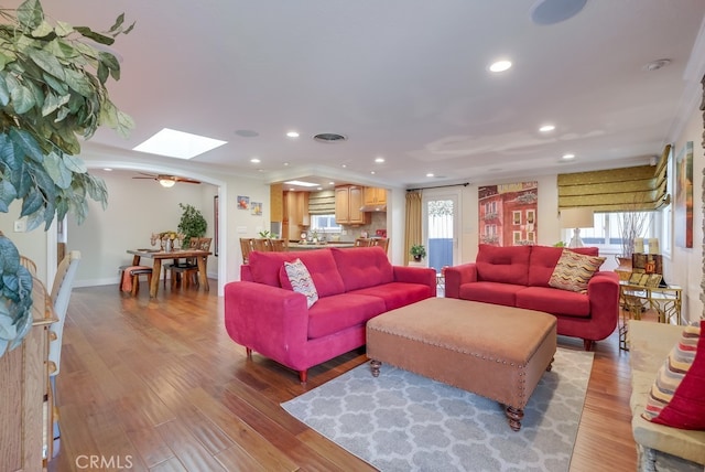 living room with crown molding, a skylight, and light wood-type flooring