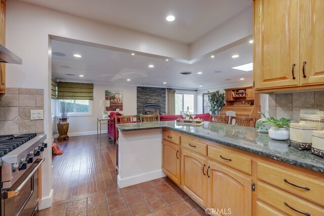 kitchen featuring kitchen peninsula, stainless steel range, backsplash, and a fireplace