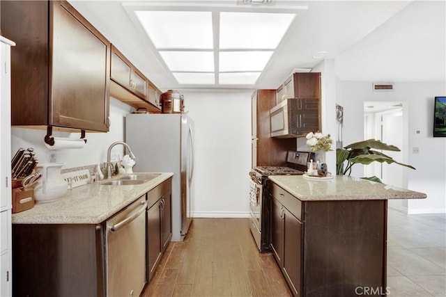 kitchen featuring light stone countertops, dark brown cabinetry, stainless steel appliances, light hardwood / wood-style floors, and sink