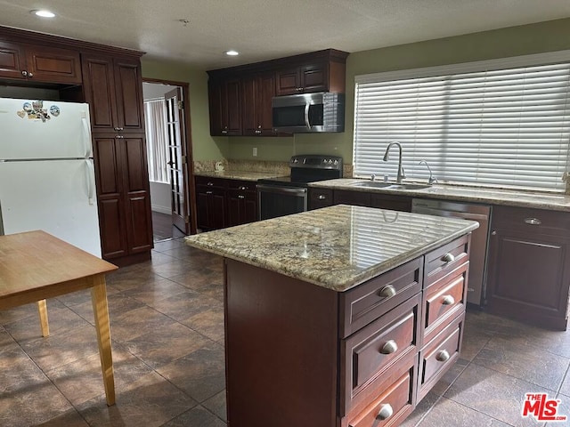 kitchen with light stone countertops, appliances with stainless steel finishes, dark brown cabinetry, sink, and a center island