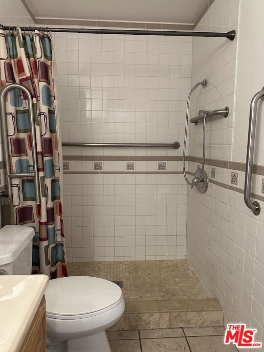 bathroom with a shower with curtain, vanity, tile walls, and toilet