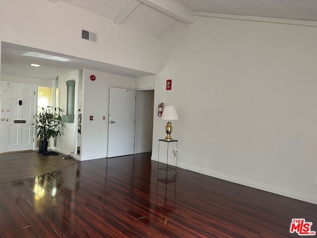 unfurnished room featuring dark hardwood / wood-style flooring, lofted ceiling with beams, and a textured ceiling