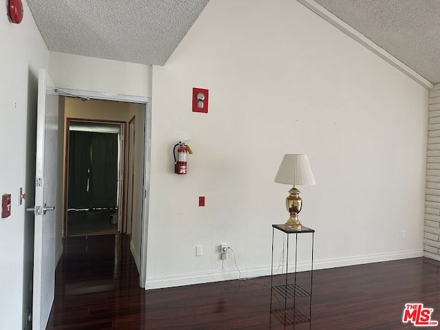 corridor featuring a textured ceiling, dark hardwood / wood-style floors, and vaulted ceiling