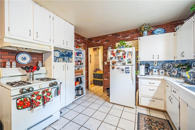 kitchen featuring light tile patterned floors, brick wall, white appliances, and white cabinetry