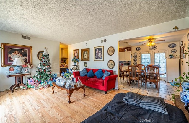 living room with ceiling fan, a textured ceiling, and light wood-type flooring