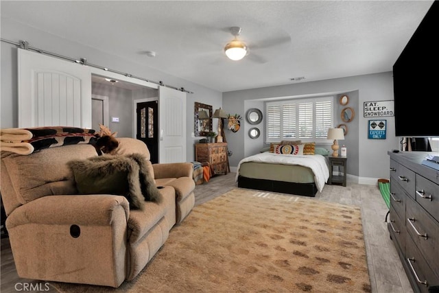 bedroom featuring light wood-type flooring, ceiling fan, and a barn door