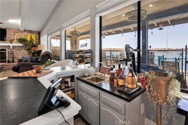 kitchen featuring white cabinets, vaulted ceiling, a brick fireplace, and sink