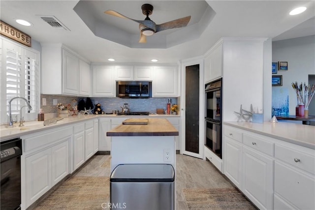 kitchen with white cabinets, black appliances, butcher block counters, a tray ceiling, and light hardwood / wood-style flooring