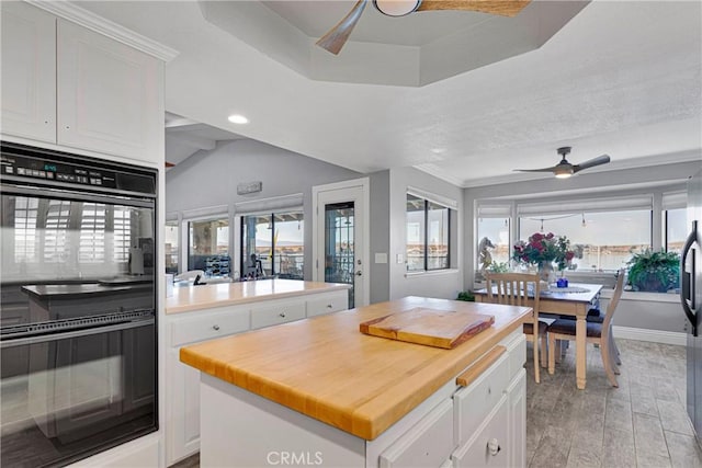 kitchen featuring ceiling fan, a kitchen island, white cabinetry, light wood-type flooring, and black double oven