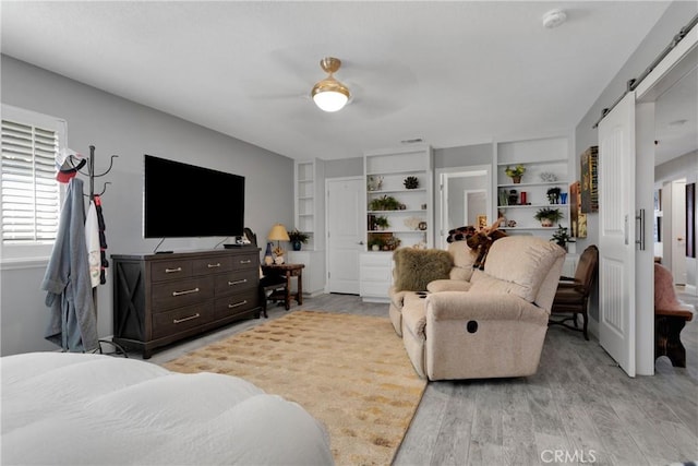 bedroom featuring ceiling fan, a barn door, and light hardwood / wood-style floors