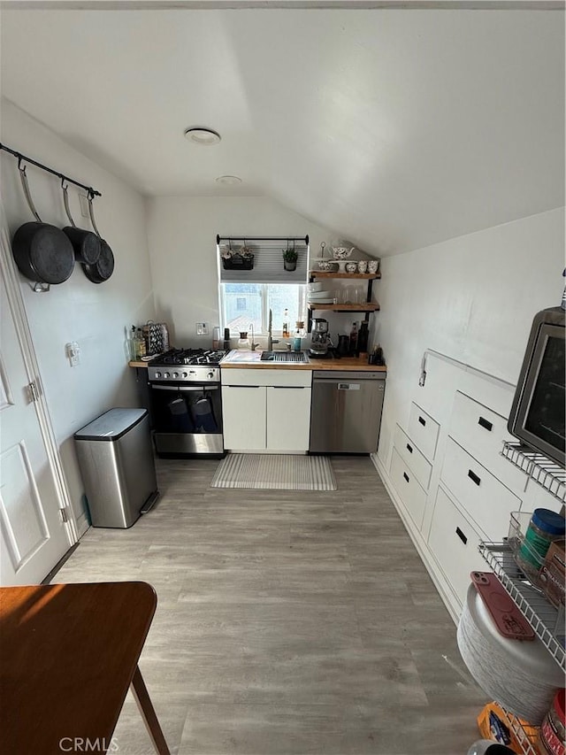 kitchen with lofted ceiling, sink, white cabinetry, light hardwood / wood-style flooring, and appliances with stainless steel finishes