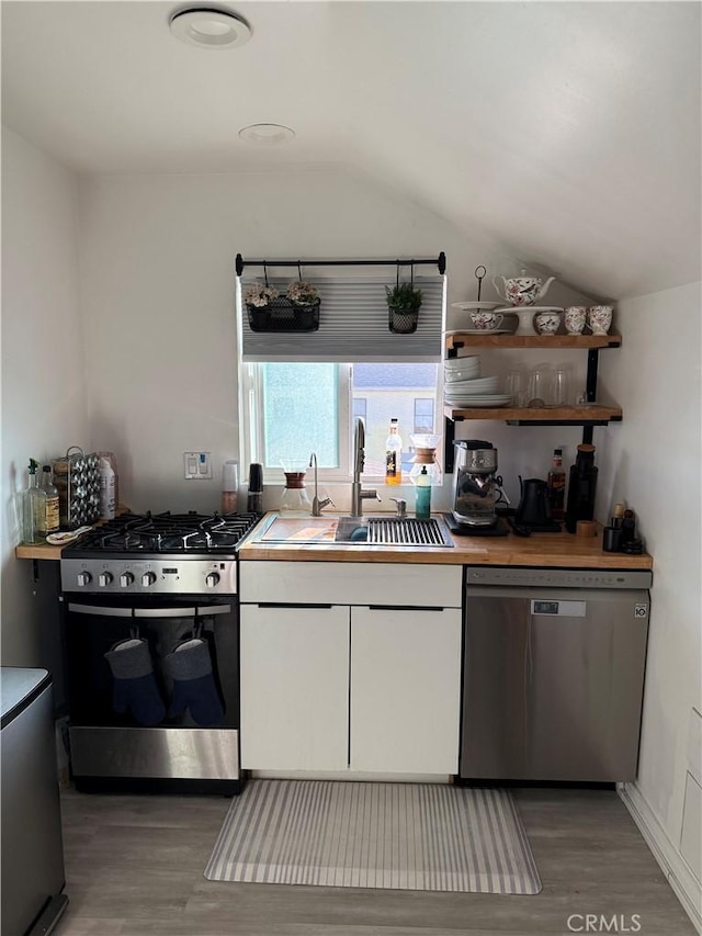 kitchen featuring white cabinets, appliances with stainless steel finishes, lofted ceiling, wood-type flooring, and sink