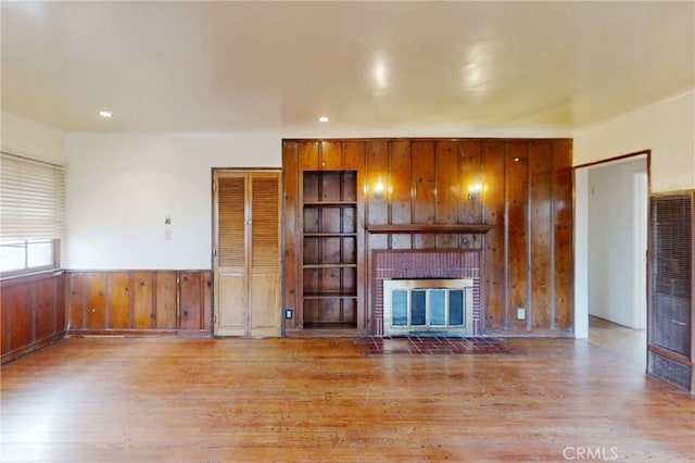 unfurnished living room featuring hardwood / wood-style flooring, a fireplace, and wood walls