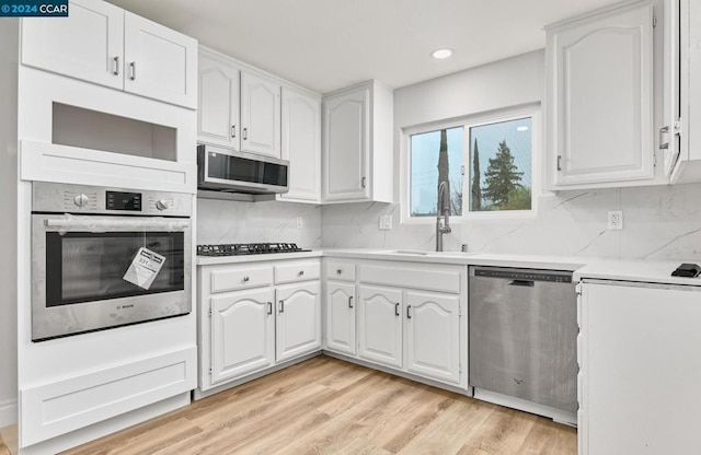 kitchen featuring stainless steel appliances, decorative backsplash, white cabinets, light hardwood / wood-style flooring, and sink