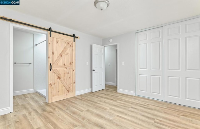 unfurnished bedroom featuring light wood-type flooring, a barn door, and a closet