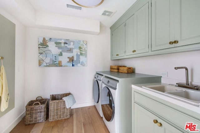 laundry room with washing machine and dryer, sink, light hardwood / wood-style floors, and cabinets