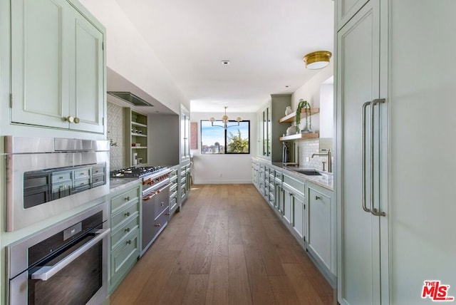 kitchen with a notable chandelier, hardwood / wood-style floors, decorative backsplash, sink, and stainless steel oven