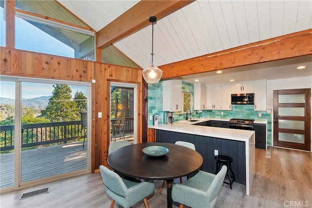 dining room featuring light wood-type flooring, a mountain view, vaulted ceiling with beams, and sink