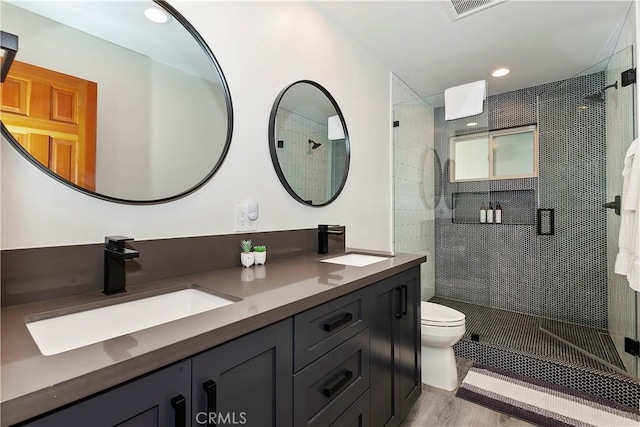 bathroom featuring toilet, tiled shower, wood-type flooring, and vanity