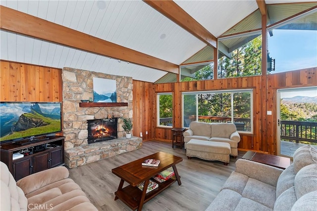 living room with light wood-type flooring, beam ceiling, a stone fireplace, and high vaulted ceiling