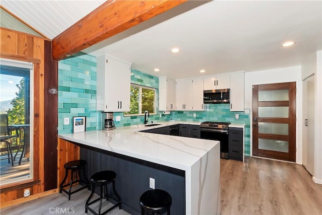 kitchen featuring white cabinets, kitchen peninsula, stainless steel appliances, and vaulted ceiling with beams