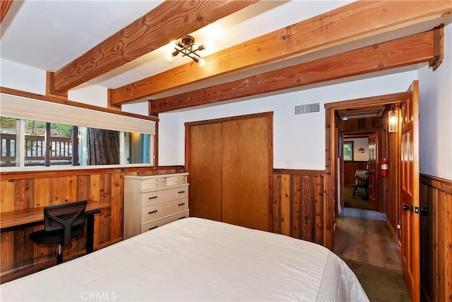 bedroom with a closet, dark wood-type flooring, beamed ceiling, and wooden walls