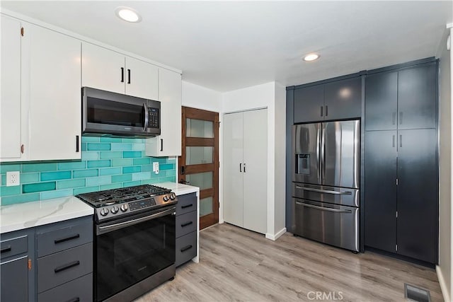 kitchen featuring white cabinets, stainless steel appliances, gray cabinets, light stone counters, and light hardwood / wood-style flooring