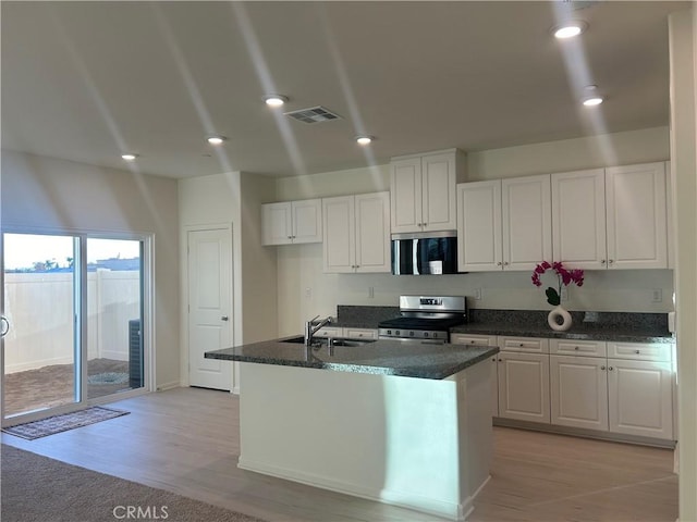 kitchen with white cabinetry, an island with sink, appliances with stainless steel finishes, dark stone counters, and sink