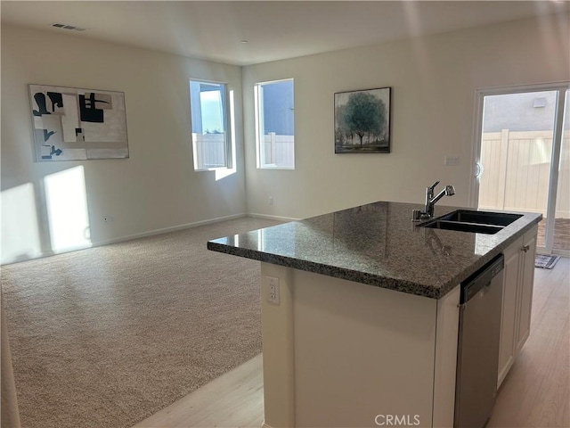 kitchen with dark stone countertops, a center island with sink, stainless steel dishwasher, sink, and white cabinetry